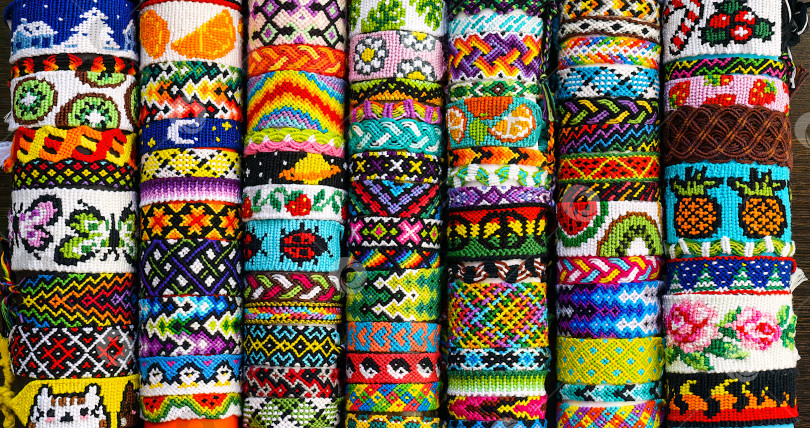 Скачать Связанный плетеный браслет дружбы своими руками с узором в виде сердечек в середине круга из множества разноцветных браслетов дружбы ручной работы из вышивки яркими нитками с узелками. фотосток Ozero