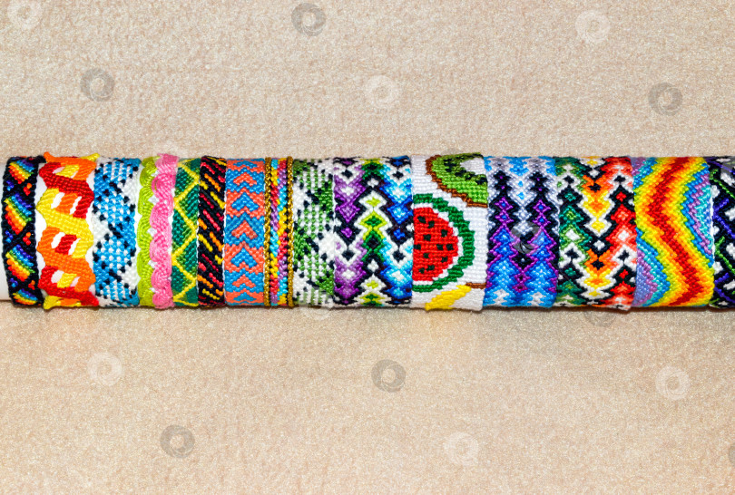 Скачать Продаются красочные плетеные браслеты дружбы ручной работы из ниток на подставке, выделенные на бежевом фоне пространством для копирования фотосток Ozero