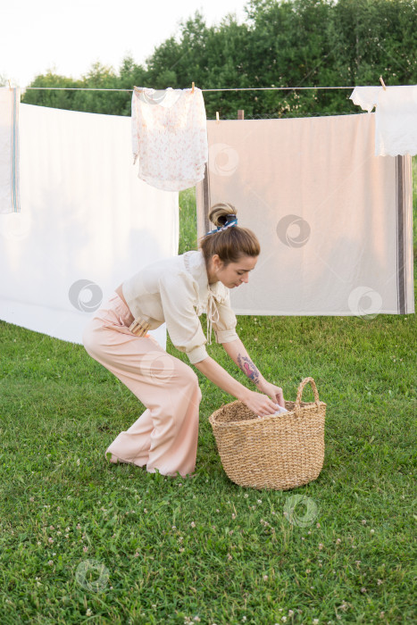 Скачать День стирки. Женщина развешивает постельное белье и полотенца на дереве во дворе деревенского дома. фотосток Ozero