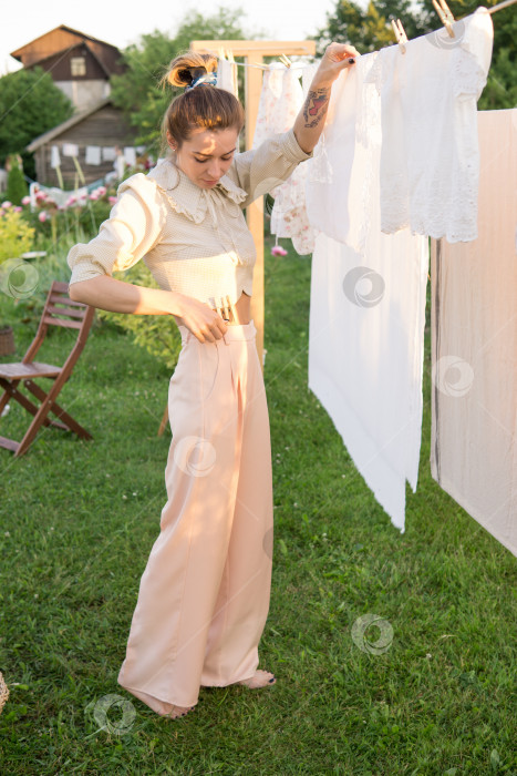 Скачать День стирки. Женщина развешивает постельное белье и полотенца на дереве во дворе деревенского дома. фотосток Ozero