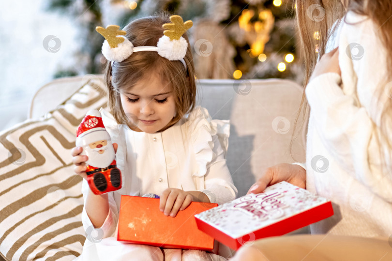 Скачать Мама и дочь малыша сидят на диване возле украшенной рождественской елки, открывают подарки.Семья. Рождественские каникулы фотосток Ozero