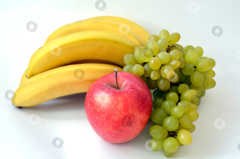 Скачать Большое красное яблоко на фоне грозди бананов и спелого индийского зеленого винограда на белом фоне фотосток Ozero