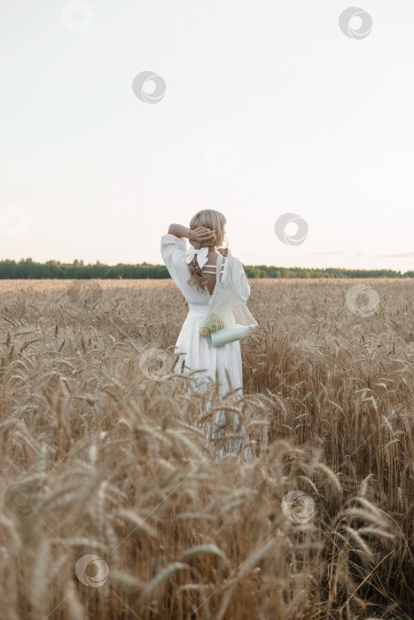 Скачать Светловолосая женщина в длинном белом платье прогуливается по пшеничному полю. Концепция свадьбы и прогулки на природе фотосток Ozero