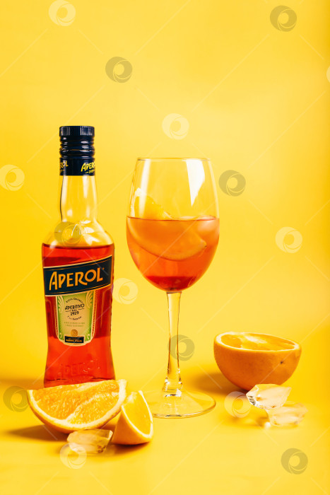 Скачать Владивосток, Россия - 21 февраля 2024 года: Бутылка летнего коктейля Aperol Aperitivo и бокал с коктейлем spritz и апельсинами на ярко-желтом фоне. фотосток Ozero