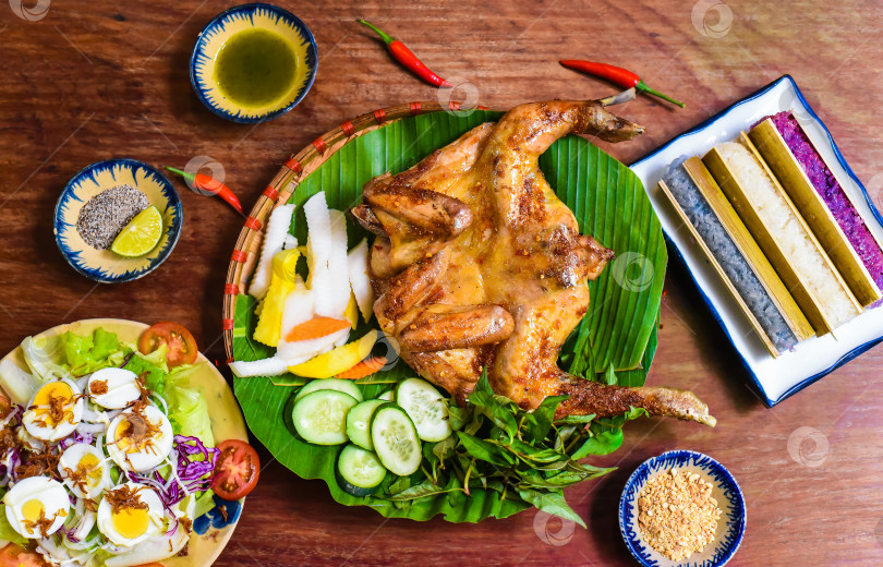 Скачать Курица-гриль по-вьетнамски с разноцветным рисом в бамбуковом соусе и вареными яйцами на деревянном столе фотосток Ozero