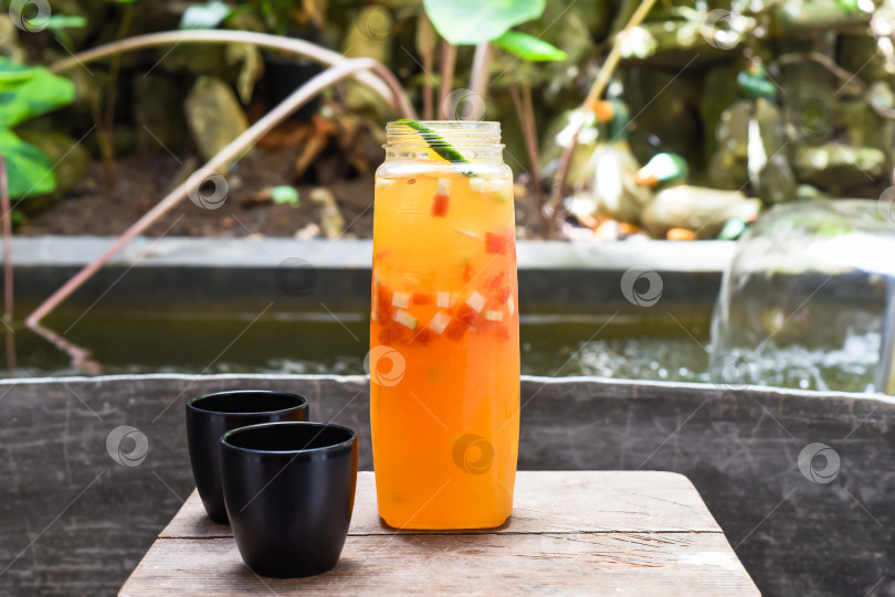 Скачать Бутылка со свежим домашним соком из апельсинов, арбуза, лайма на деревянном столе с чашками фотосток Ozero