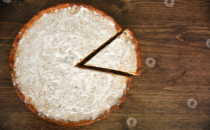 Скачать Ломтик домашнего пирога с лимонно-апельсиновой начинкой, посыпанный сахарной пудрой, на деревянном столе. скопировать с места фотосток Ozero