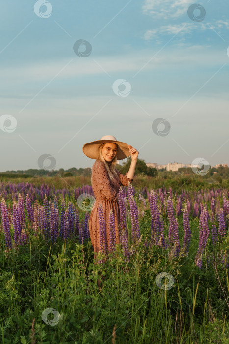 Скачать Красивая женщина в соломенной шляпе прогуливается по полю с фиолетовыми цветами. Прогулка на природе по полю люпина фотосток Ozero
