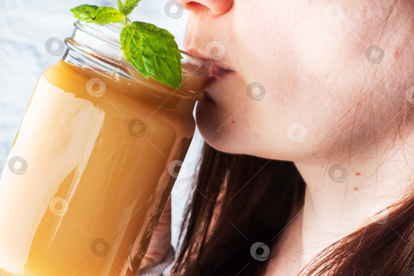 Скачать Молодая девушка держит в руке стеклянную кружку с соком и пьет. Свежевыжатый сок с мятой. Особое внимание уделяется выбору. фотосток Ozero