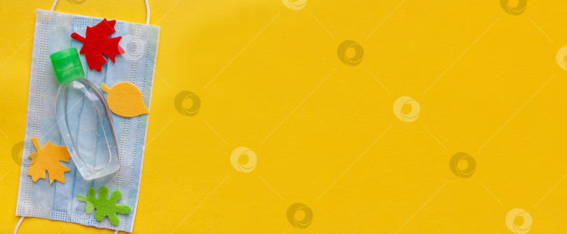 Скачать На защитной маске лежит дезинфицирующее средство, окруженное войлочными осенними листьями на желтом фоне. Плашмя лежал. Вид сверху. фотосток Ozero