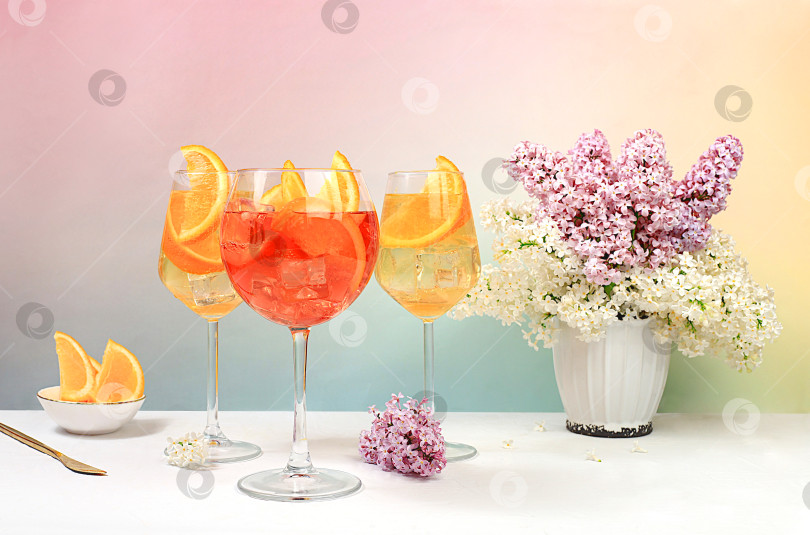 Скачать Праздничный алкогольный коктейль Aperol spritz в бокалах на ярком фоне с букетом сирени, концепция летнего бара, алкогольные напитки на вечеринке, реклама ресторанов и кафе, фотосток Ozero