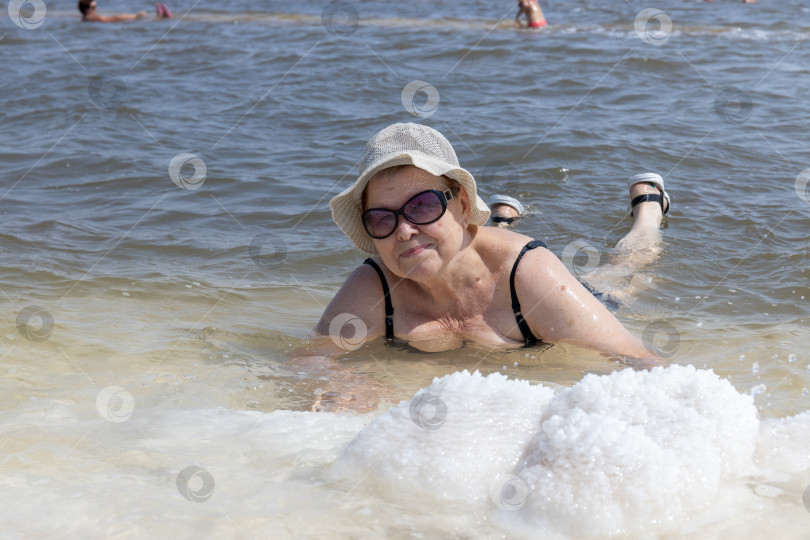 Скачать пожилая дама в очках и панаме с улыбкой на лице загорает на соленом озере Баскунчак в Астраханской области России фотосток Ozero