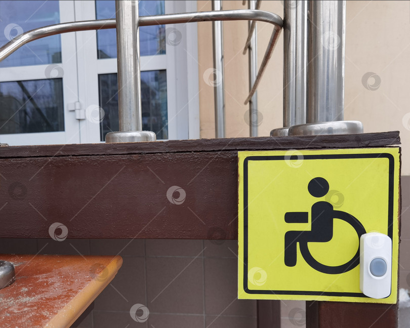 Скачать Знак доступности для инвалидных колясок (изображение человека в инвалидной коляске на желтом фоне) у входа в магазин. рядом установлена кнопка помощи. фотосток Ozero