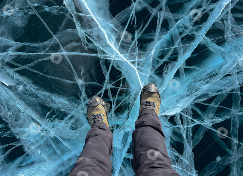 Скачать Нога туриста, стоящего на растрескавшейся поверхности замерзшего озера Байкал в зимний сезон в Сибири, Россия фотосток Ozero