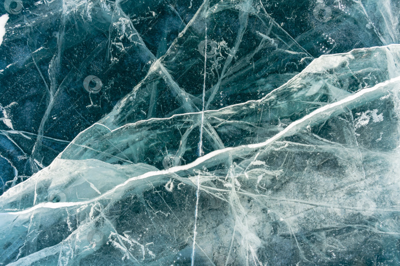 Скачать Естественная текстура зимнего льда с белыми пузырьками и трещинами на замерзшем озере. Абстрактный фон из льда и трещин на поверхности замерзшего озера Байкал. фотосток Ozero