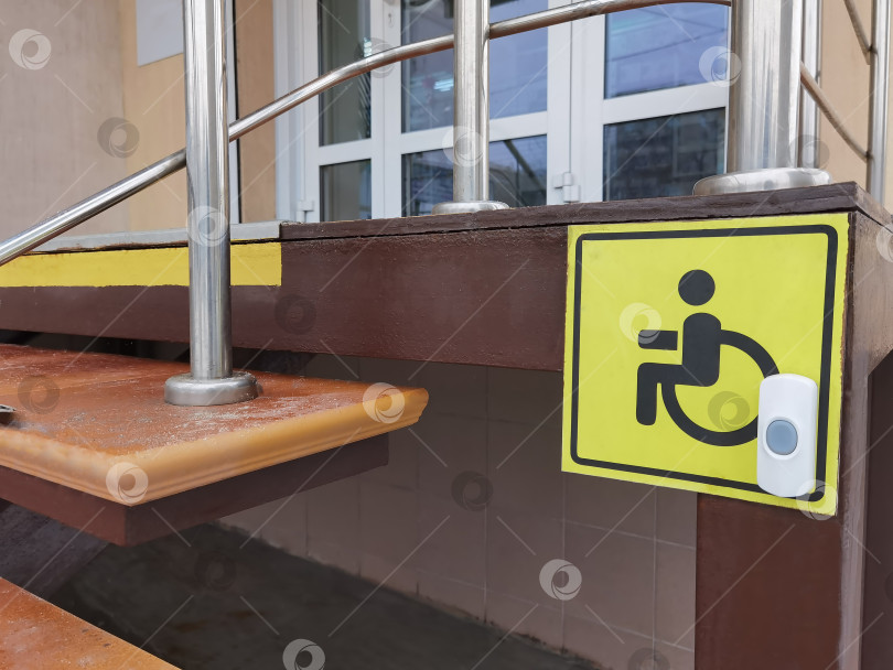 Скачать Знак доступности для инвалидных колясок (изображение человека в инвалидной коляске на желтом фоне) у входа в магазин. рядом установлена кнопка помощи. фотосток Ozero