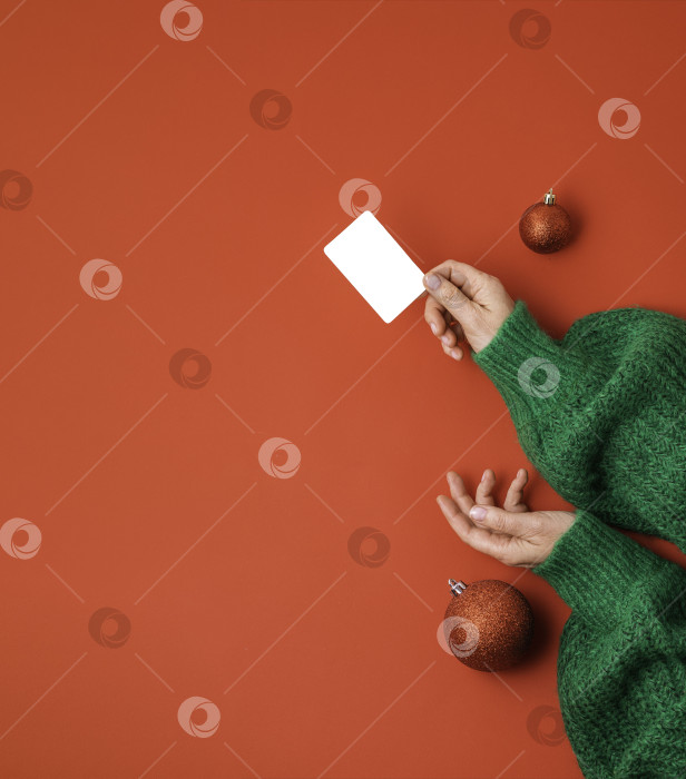Скачать Концепция рождественских покупок. Руки в зеленом свитере с бонусной картой лежат ровно. Баннер на красном фоне фотосток Ozero