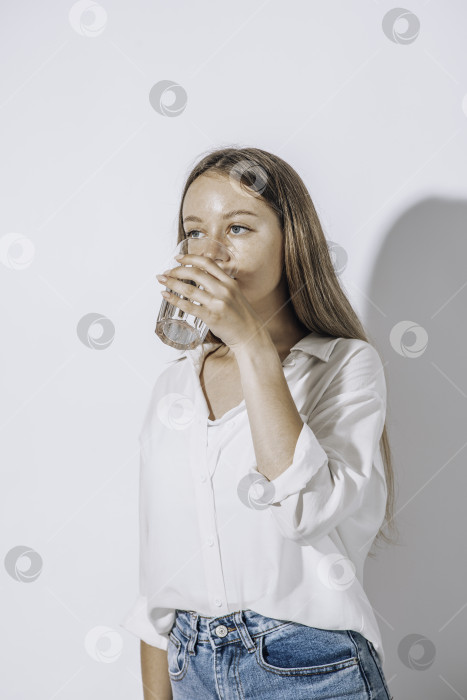 Скачать Девушка пьет воду из стеклянного стакана на белом фоне. Концепция поддержания водного баланса фотосток Ozero