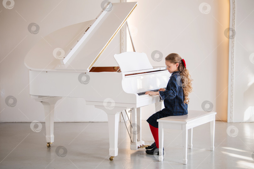 Скачать Маленькая девочка играет на большом белом пианино в светлой солнечной комнате фотосток Ozero