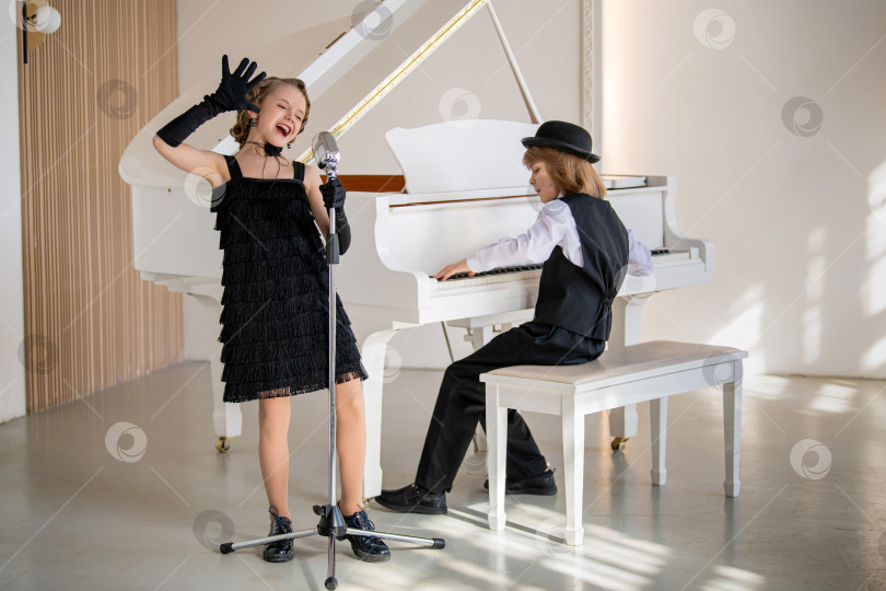 Скачать Молодая девушка в черном платье поет в микрофон, а мальчик играет на пианино. фотосток Ozero
