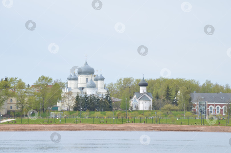 Скачать Великий Новгород, Россия - 13.05.2024: Вид на Зверин-Покровский дворец в Великом Новгороде со сторо-ны рек Волхов: Покровский собор (рубеж XIX-XX вековъ) и Симеоновская церковь (Церковь Симеона Богоприимца XV века) фотосток Ozero