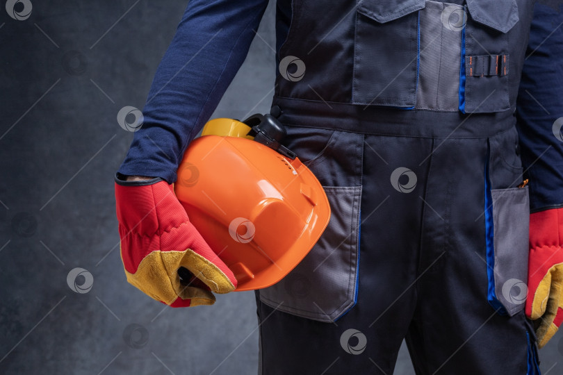Скачать Крупный план рабочего, строителя, держащего каску на фоне темной стены. фотосток Ozero