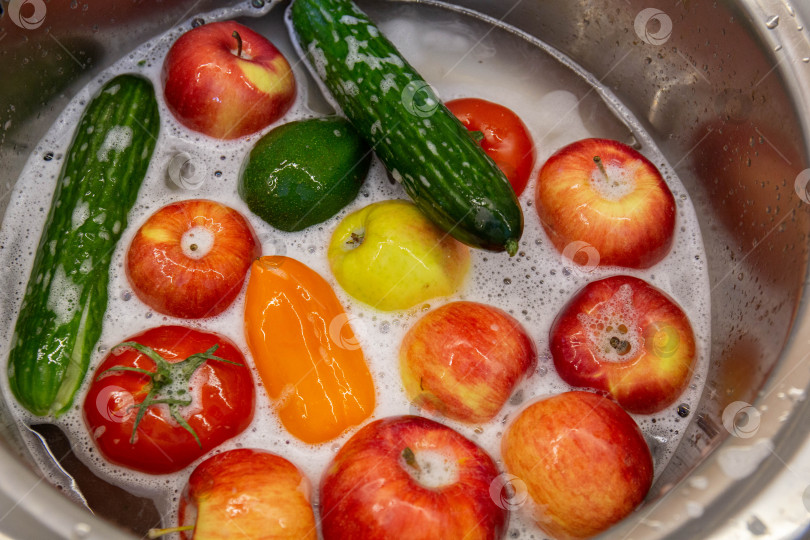Скачать Много разноцветных фруктов: огурцы, яблоки, помидоры и другие в кухонной раковине под струей воды фотосток Ozero