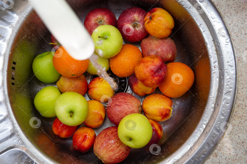 Скачать Много разноцветных фруктов: апельсины, яблоки, нектарины в кухонной раковине под струей воды фотосток Ozero