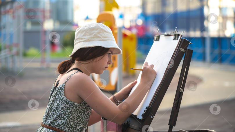 Скачать Симпатичная девочка-подросток рисует за мольбертом на открытом воздухе фотосток Ozero