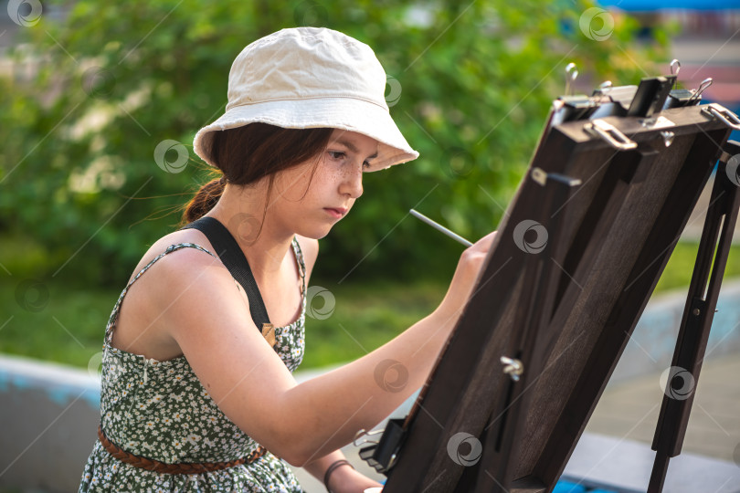 Скачать Симпатичная девочка-подросток рисует за мольбертом на открытом воздухе фотосток Ozero