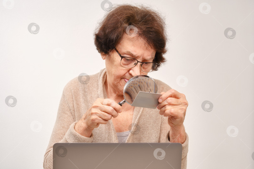 Скачать Пожилая женщина в очках делает покупки онлайн, используя свой ноутбук и кредитную карту. фотосток Ozero
