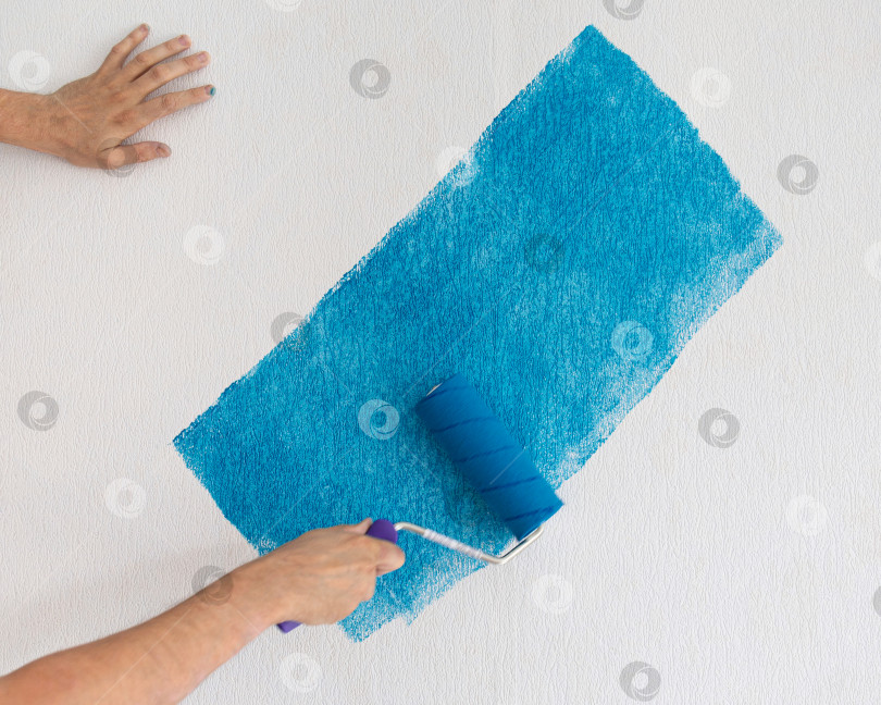 Скачать Мужчина раскрашивает белую стену синей краской с помощью валика фотосток Ozero