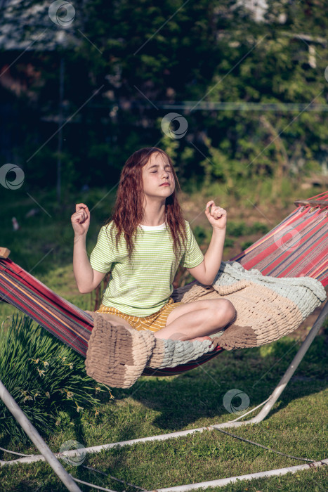 Скачать симпатичная рыжеволосая девочка-подросток сидит в гамаке в позе лотоса фотосток Ozero