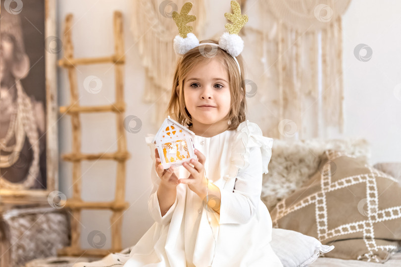 Скачать Портрет маленькой девочки-малыша с повязкой на голове в виде оленьих рогов и рождественской игрушкой в руках. Рождественские каникулы.Легкий и яркий фотосток Ozero