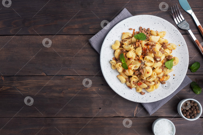 Скачать Тушеные макароны с говяжьим фаршем и овощами, макароны по-флотски на тарелке. Фон из темного дерева. Скопируйте пространство. фотосток Ozero