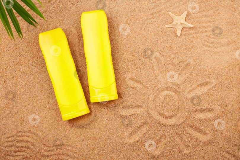 Скачать Тюбики солнцезащитного крема и пальмовый лист на песке на пляже. фотосток Ozero