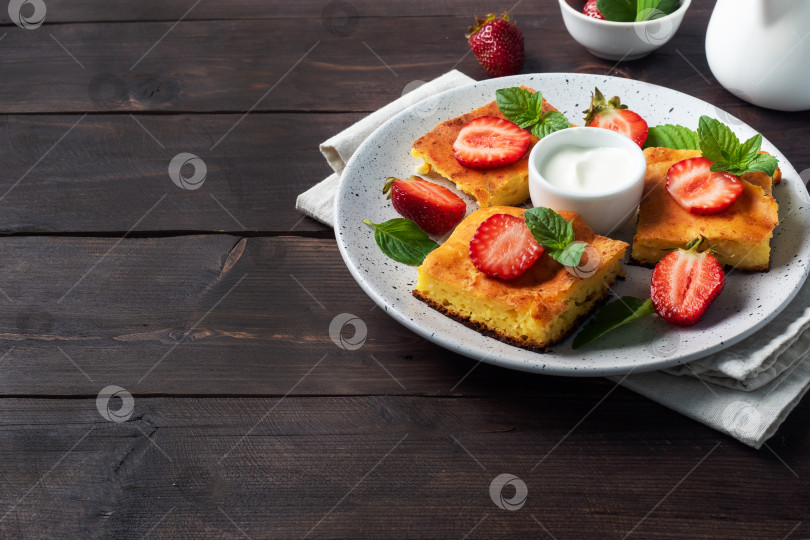 Скачать Творожная запеканка с клубникой и мятой. Вкусный домашний десерт из творога и свежих ягод со сливками. фон из темного дерева, копия пространства. фотосток Ozero