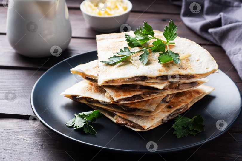 Скачать Кусочки кесадильи с грибами, сметаной и сыром на тарелке, украшенной листьями петрушки. Деревянный фон крупным планом. фотосток Ozero