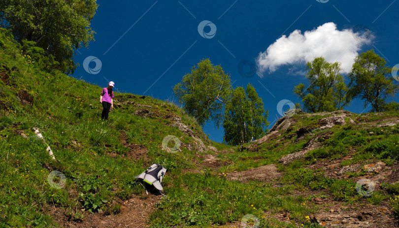 Скачать Турист, любующийся видом с тропы, заросшей пышной растительностью на склоне холма. фотосток Ozero