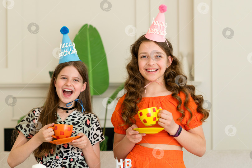 Скачать Две девочки в праздничных шапочках смеются и держат в руках чашки фотосток Ozero