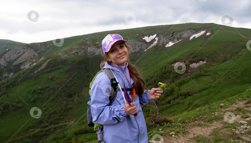 Скачать Улыбающийся молодой турист с цветами в руках на горной тропинке. фотосток Ozero