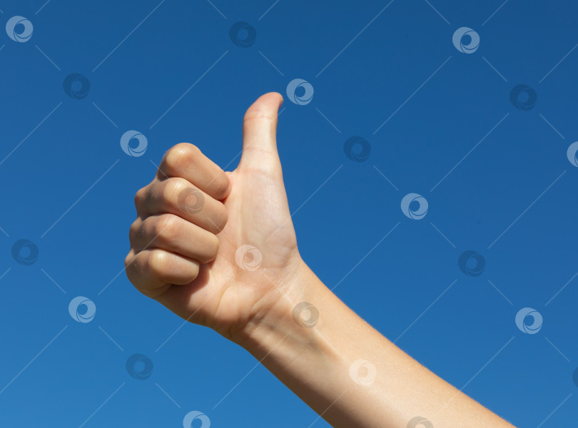 Скачать Девочка-подросток показывает поднятый большой палец на фоне голубого безоблачного неба, концепт на тему "все в порядке" фотосток Ozero