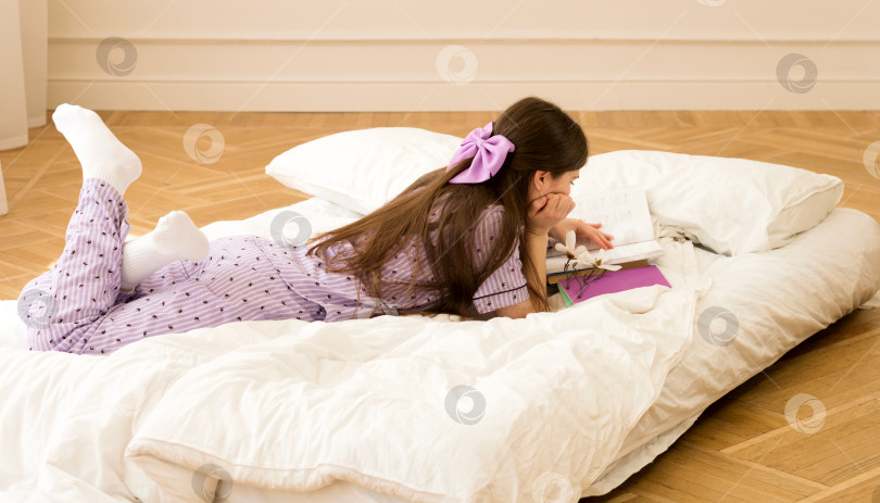 Скачать Girl in purple pajamas reading books on bed фотосток Ozero