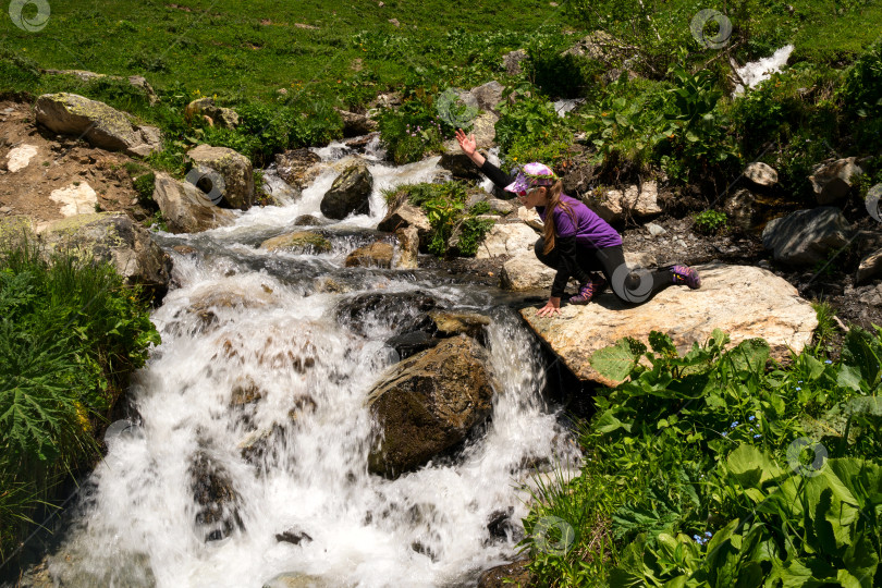 Скачать Девушка машет рукой, исследуя горный ручей со скалы. фотосток Ozero