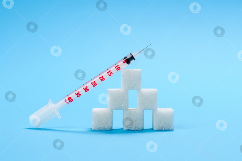 Скачать Инсулиновый шприц лежит на пирамиде из белых кубиков сахара на синем фоне. Концепция сахарной зависимости и развития сахарного диабета. фотосток Ozero