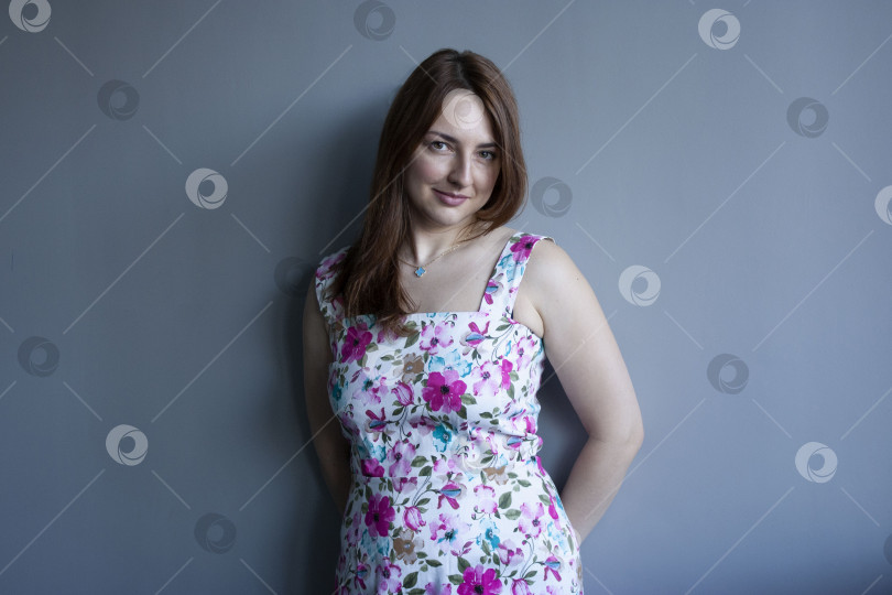 Скачать Молодая красивая счастливая женщина европейской внешности в платье на фоне однотонной серой стены фотосток Ozero