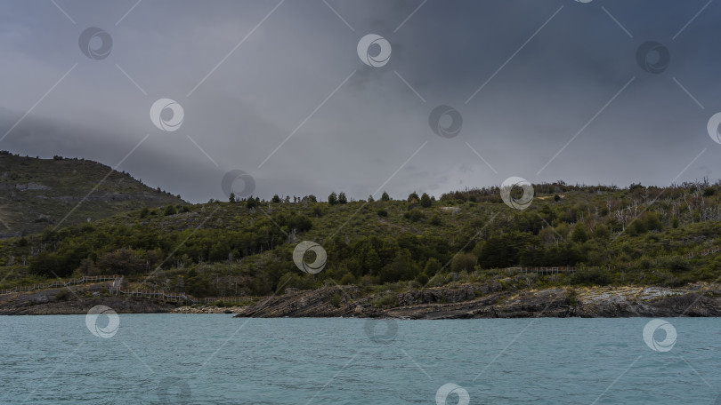 Скачать Бирюзовое ледниковое озеро. На прибрежных холмах растет лес. фотосток Ozero