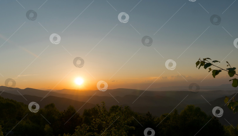Скачать Солнце садится над горами и лесистым ландшафтом. фотосток Ozero