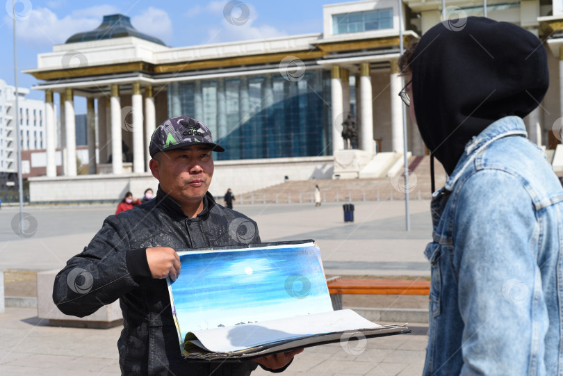 Скачать Улан-Батор, Монголия - 05.11.2022: Монгольский мужчина показывает туристу сувениры на продажу фотосток Ozero