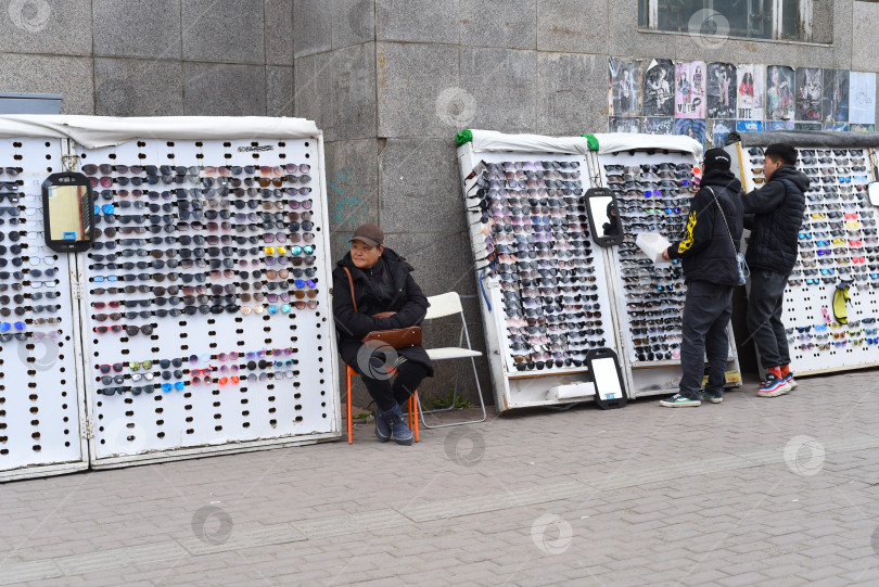 Скачать Улан-Батор, Монголия - 13.05.2022: пожилая женщина в Монголии продает солнцезащитные очки на улице фотосток Ozero